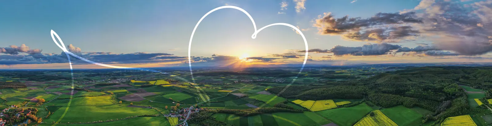 Luftaufnahme der Landschaft um Craheim bei Sonnenuntergang: Felder, Rapsblüte, Wald und weiter Himmel, mit gezeichnetem Herz